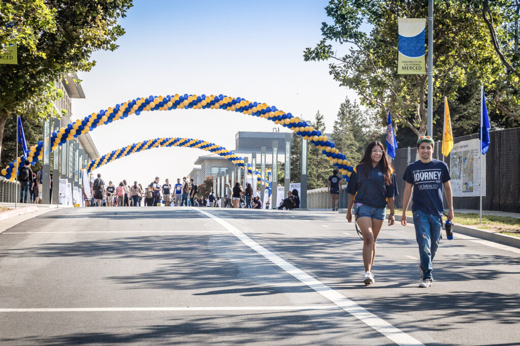 UC Merced students walking past blue-and-gold welcome arches on campus – featured image from the EdSource coverage.