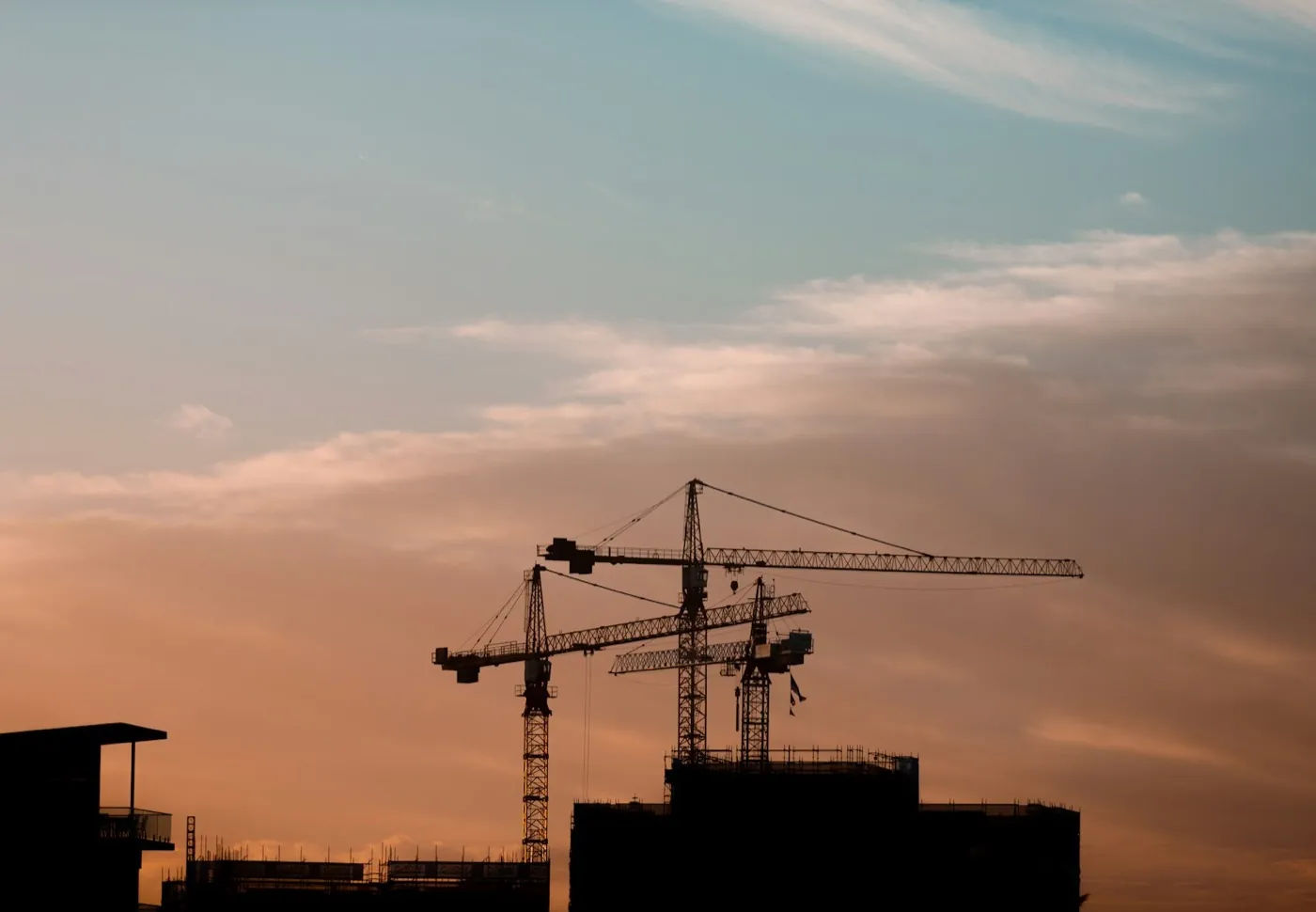 Three tower cranes silhouetted over a building under construction at dusk – the development and construction phase of the real estate lifecycle. Stand-in (Unsplash, Tye Doring; see public/assets/platform/LICENSES.md).