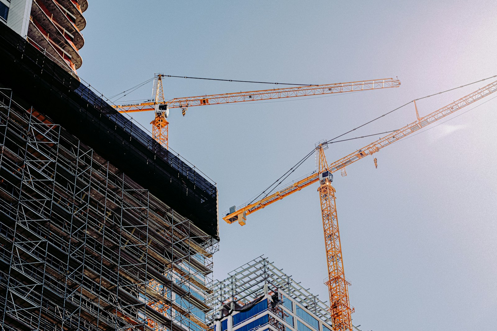 Yellow construction crane positioned near a high-rise during daytime in Los Angeles – Bobby's HOME-P2 thematic spec for Development ('buildings being built'). Finalised stand-in (Unsplash, Frames For Your Heart; see public/assets/platform/LICENSES.md).
