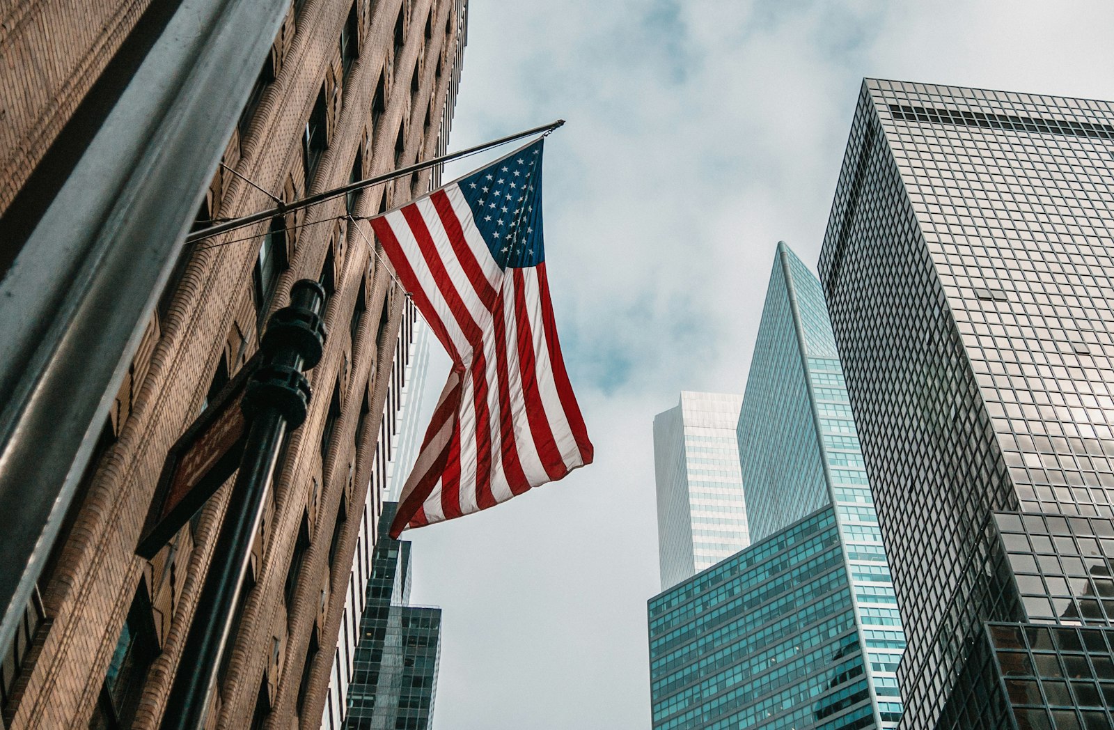 Low-angle view of the American flag flying among financial-district towers under a bright sky – the US investment destination behind the EB-5 program.
