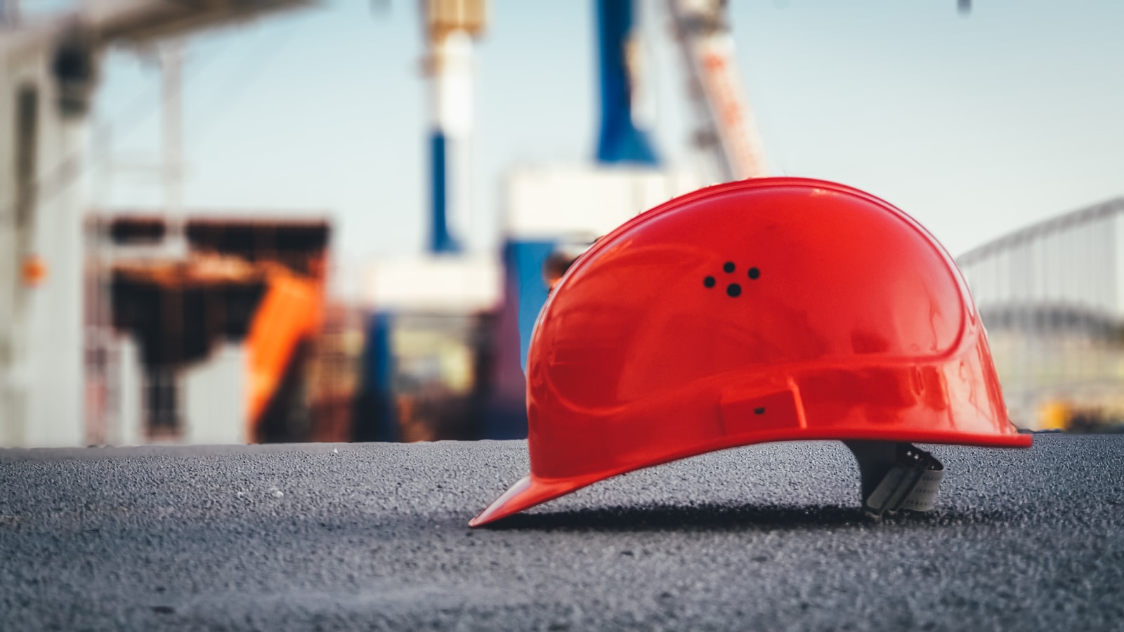 A solitary red hard hat resting on pavement, composed as a 'Safety first' still life – Bobby's HOME-P2 thematic spec for Insurance ('reference to safety'). Finalised stand-in (Unsplash, Ümit Yıldırım; see public/assets/platform/LICENSES.md).